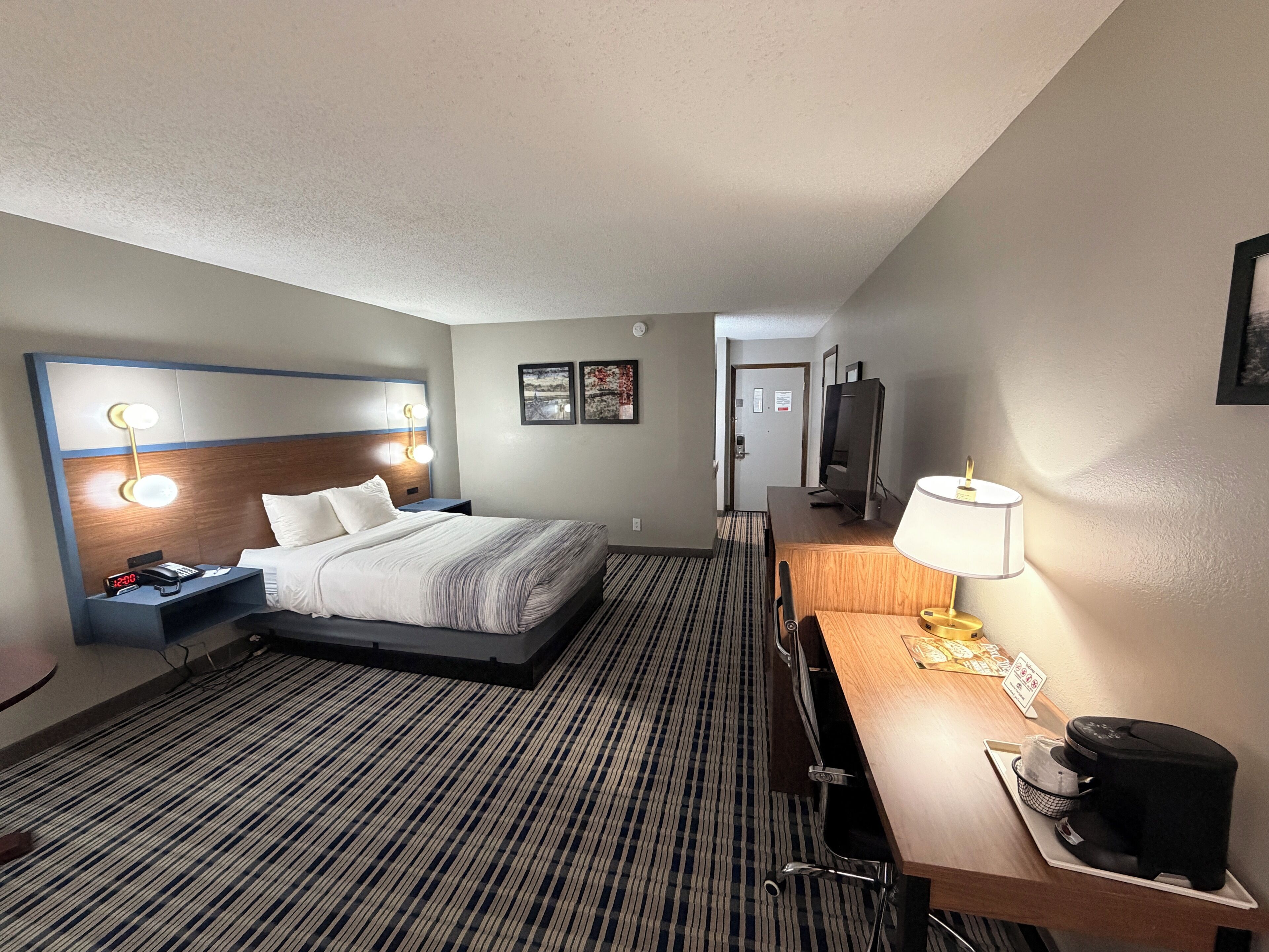 Une chambre d’hôtel comprenant un lit, une table de chevet, une lampe, une télévision et un bureau avec une chaise.