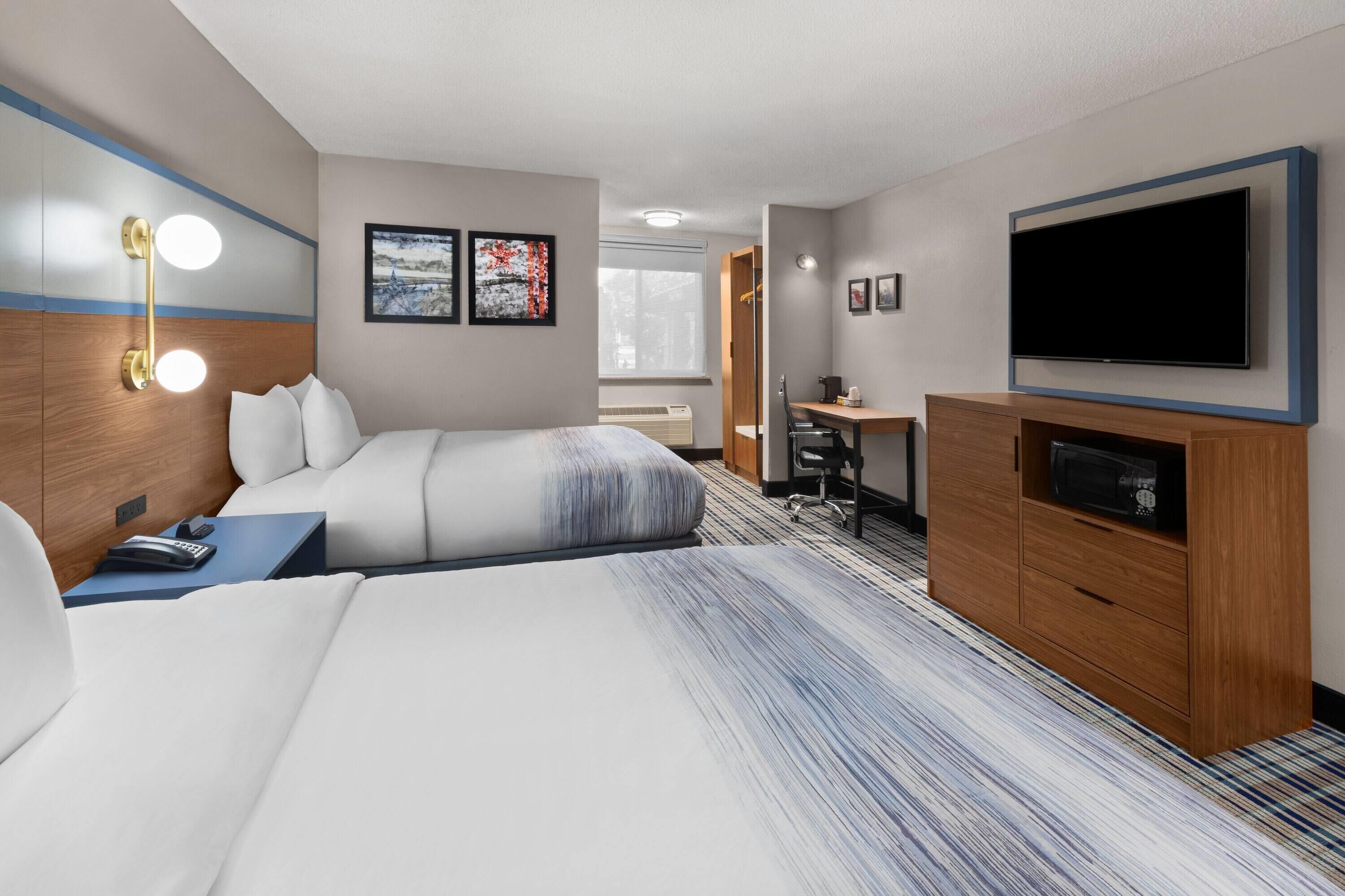 A hotel room with two beds, a desk, a television, and artwork on the walls.
