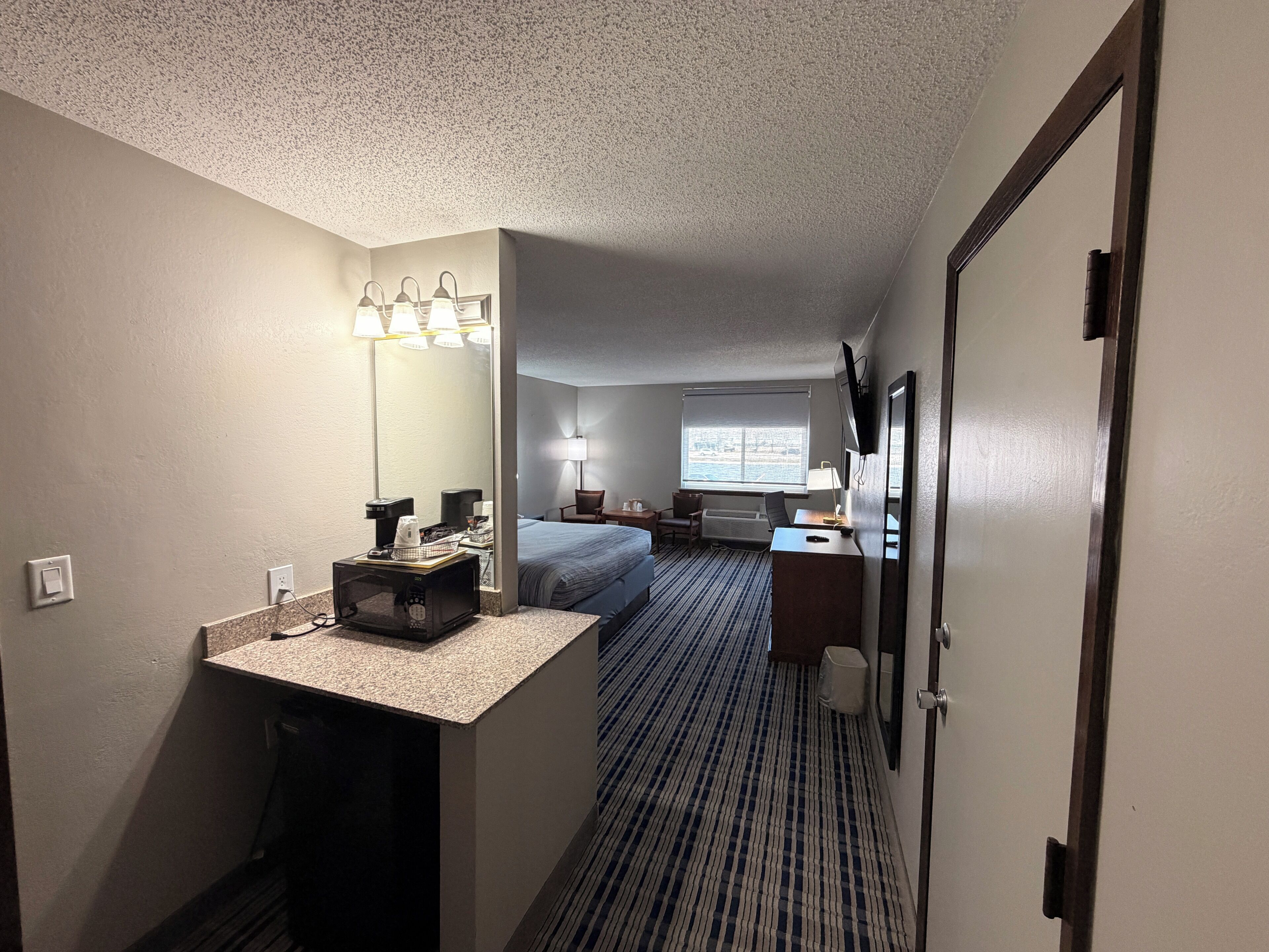 A hotel room with a bed, desk, mirror, and a window with a view.