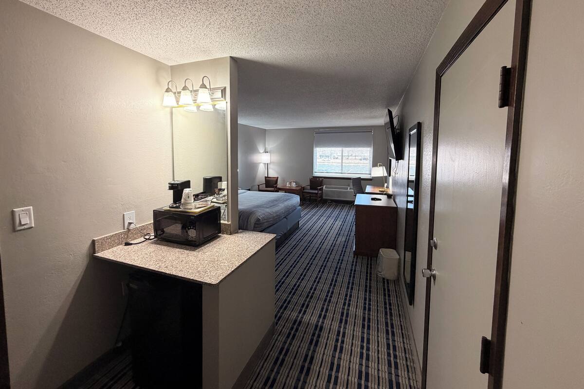 A hotel room with a bed, desk, mirror, and a window with a view.