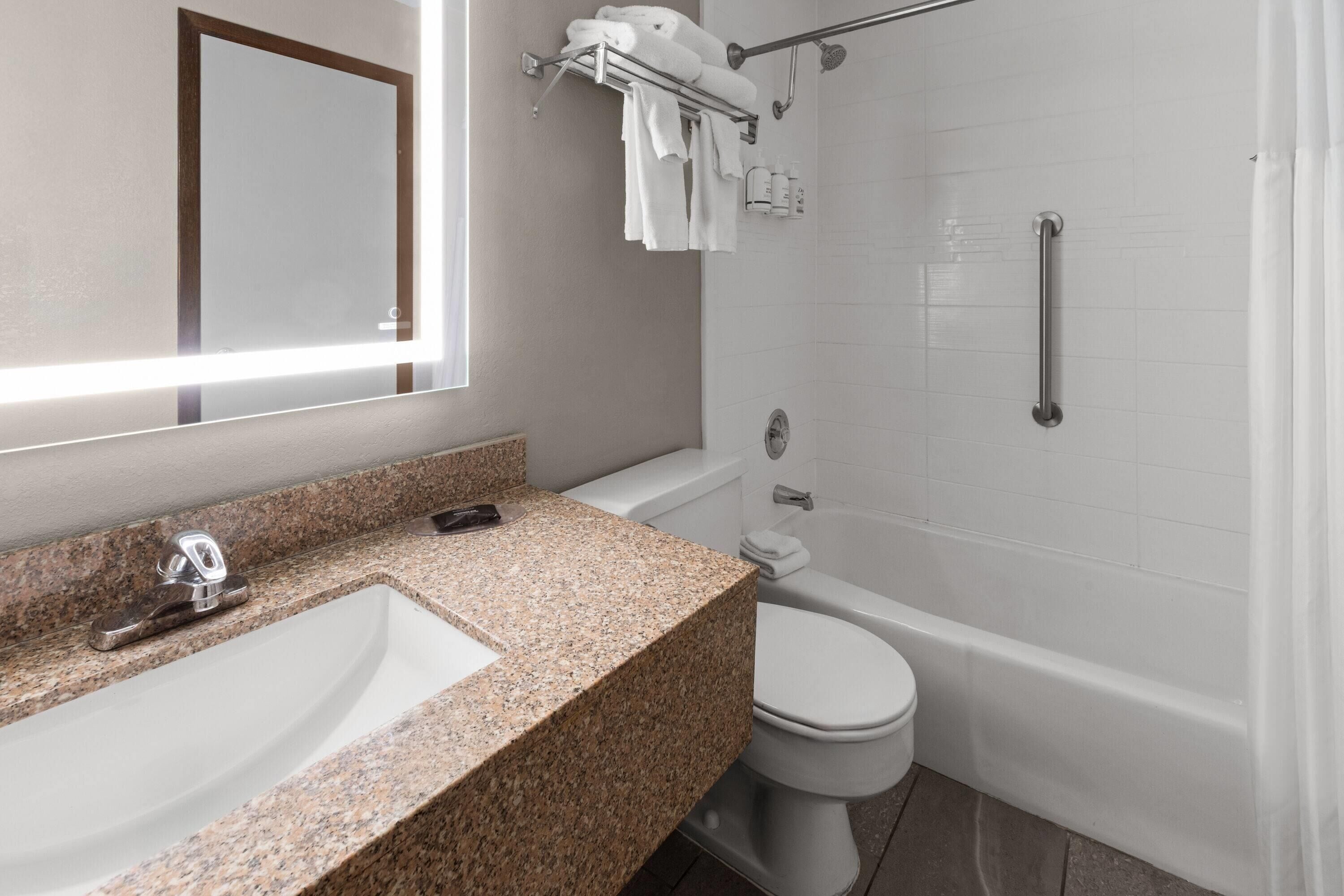 A bathroom with a granite countertop sink, a white toilet, a bathtub, and a shower with a grab bar.