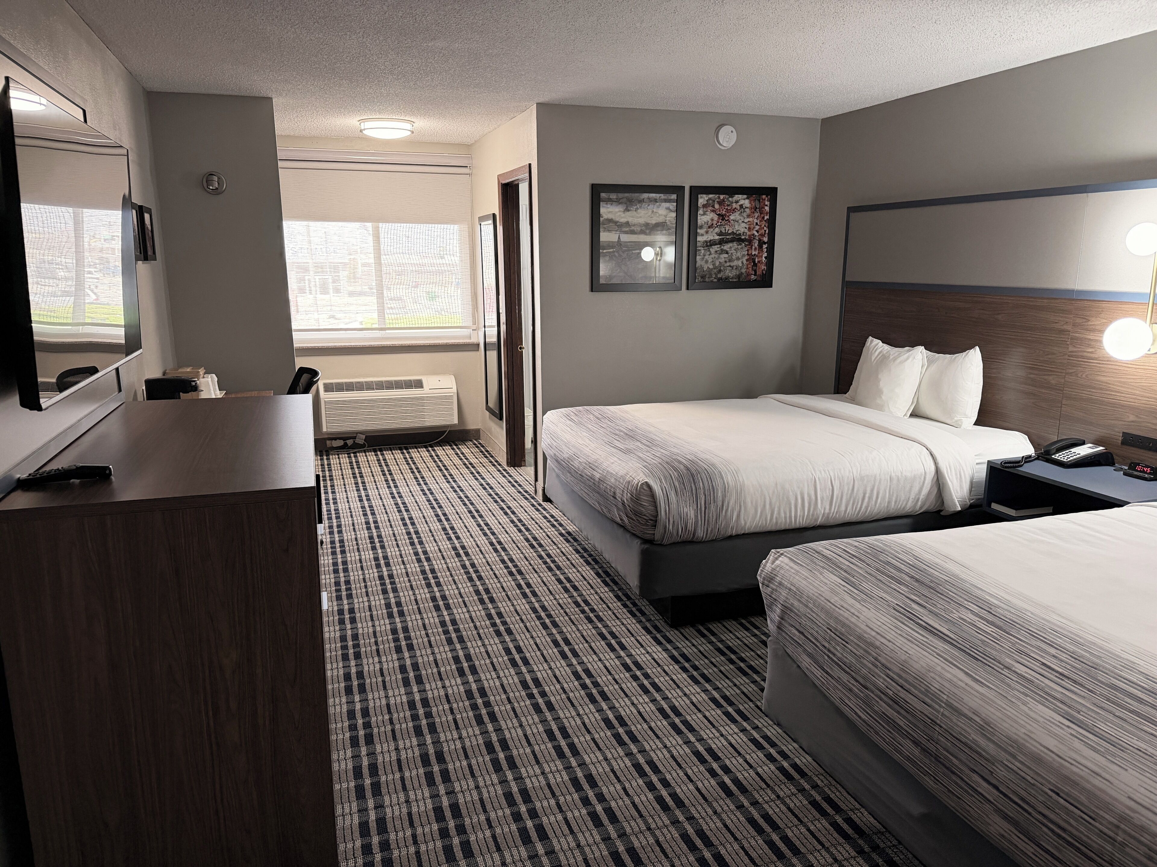 A hotel room with a bed, bedside table, TV, and a window with blinds.