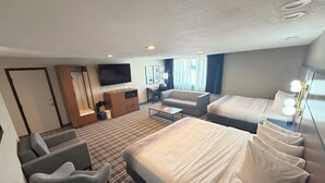 Habitación de hotel con cama, sofá, escritorio, televisor y ventana con cortinas.
