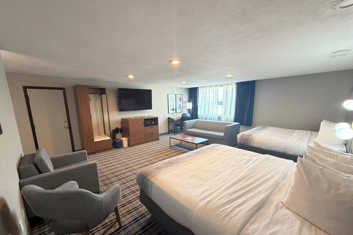 A hotel room with two beds, a sofa, a desk, a TV, and a window with curtains.