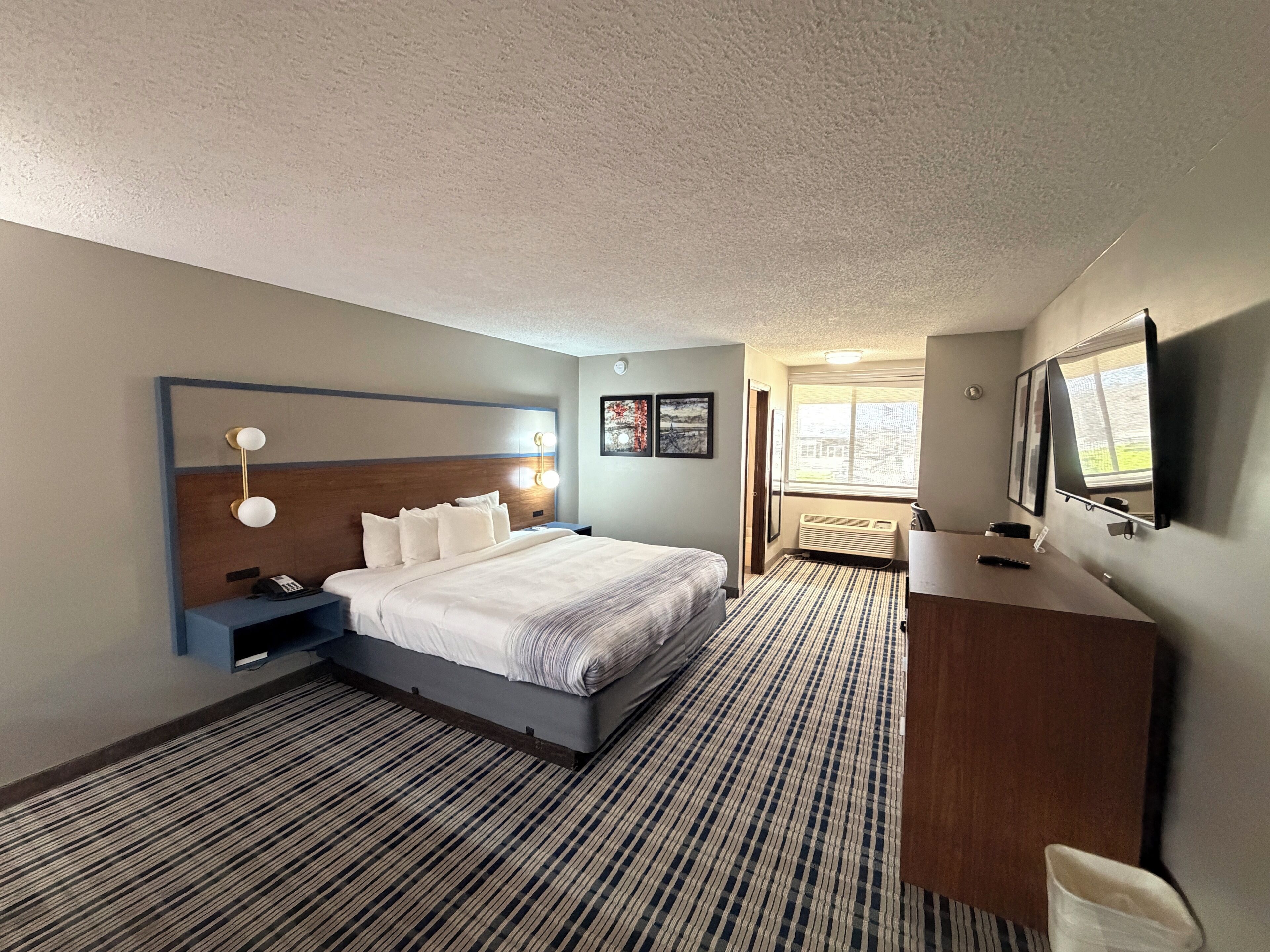 Habitación de hotel con cama, mesita de noche, lámpara, escritorio, silla y televisor.