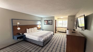 A hotel room with a bed, bedside table, lamp, desk, chair, and a TV.