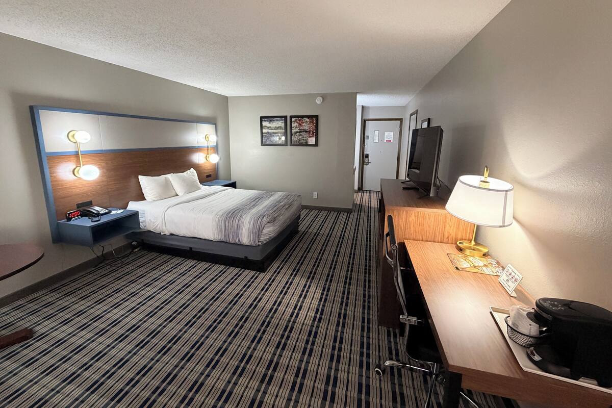 A hotel room with a bed, bedside table, lamp, desk, chair, and a television.