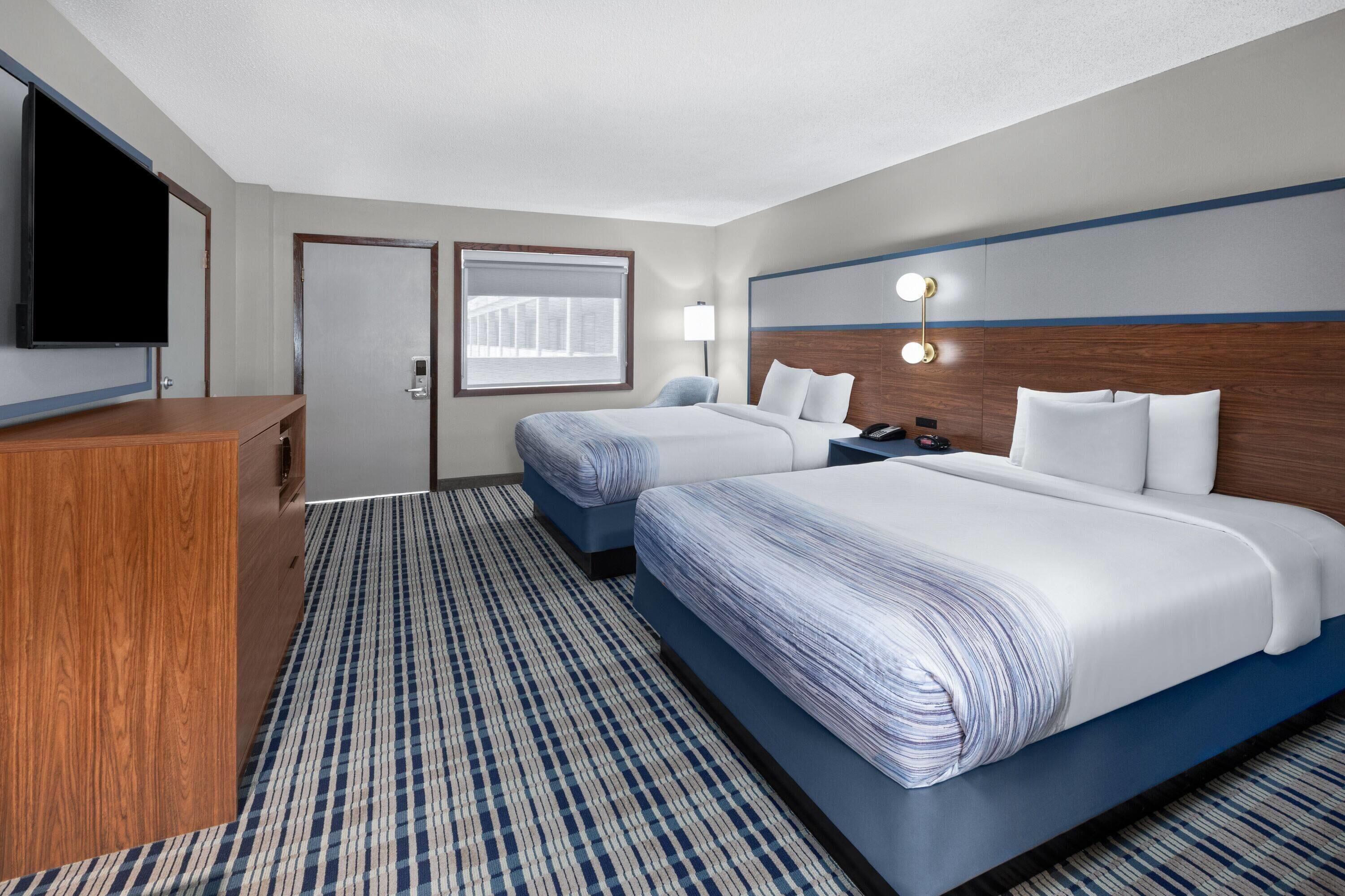 Une chambre d’hôtel avec deux lits, un bureau, une télévision et une fenêtre avec des stores.