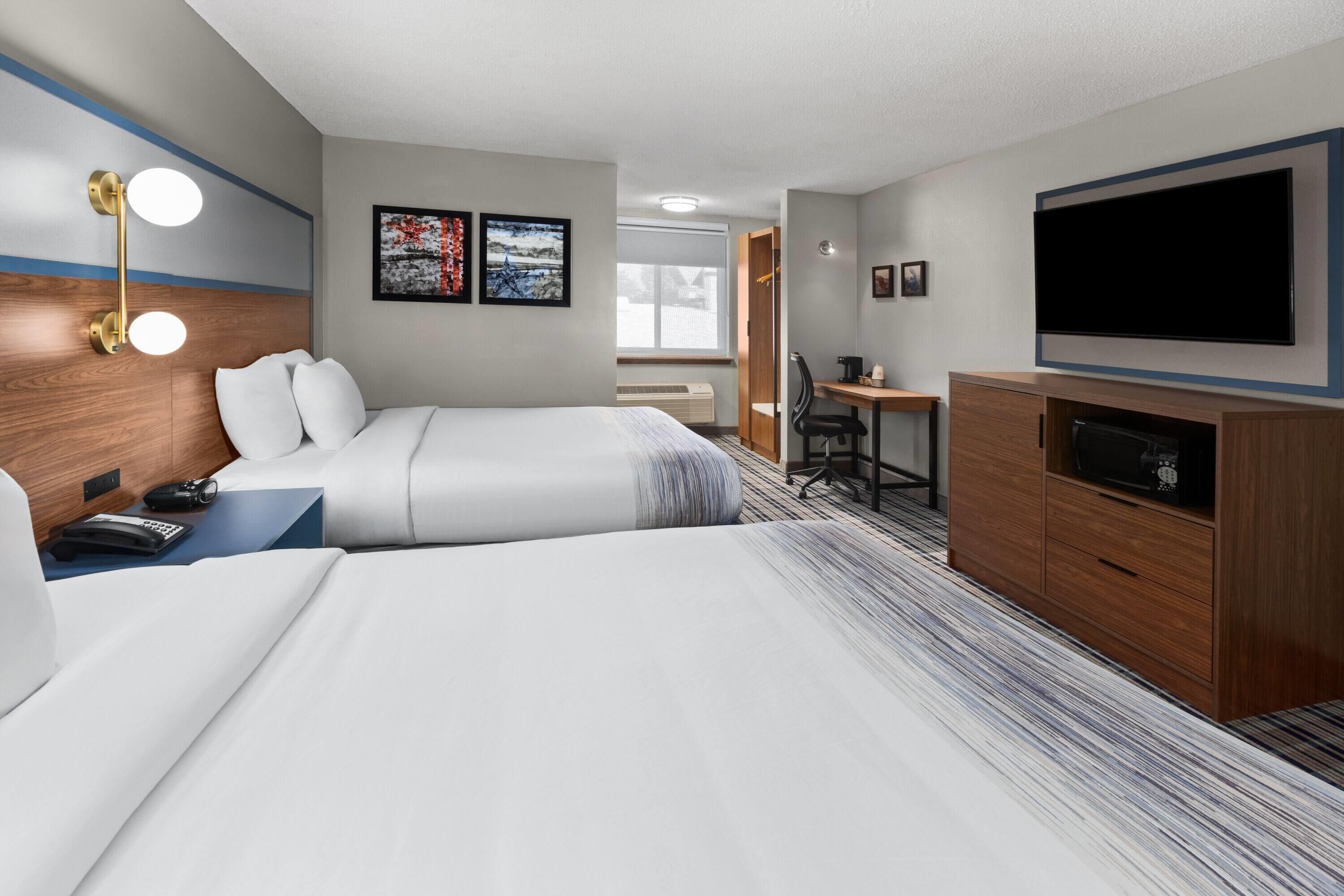 A hotel room with two beds, a desk, a television, and artwork on the wall.