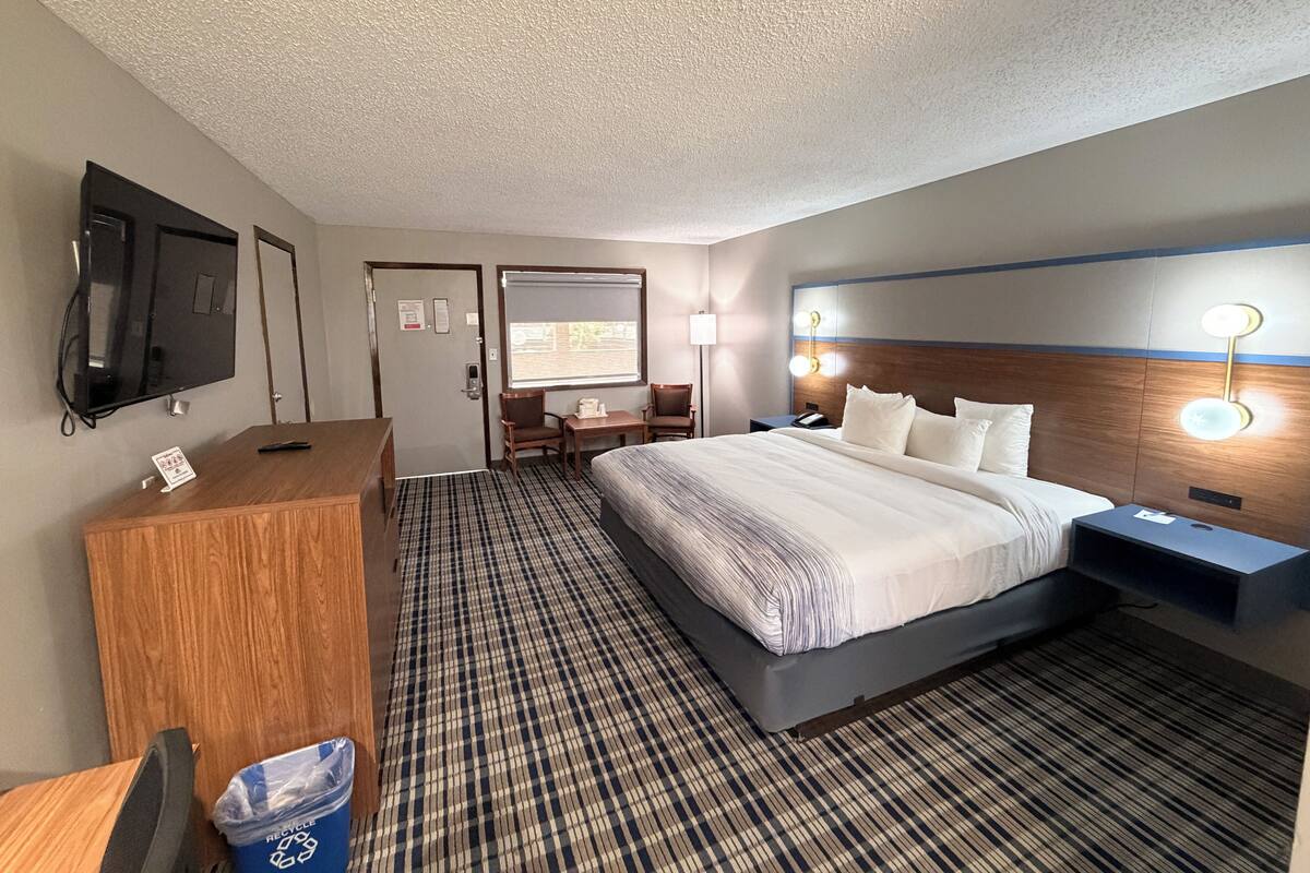 A hotel room with a bed, desk, chair, television, and a wall-mounted light fixture.