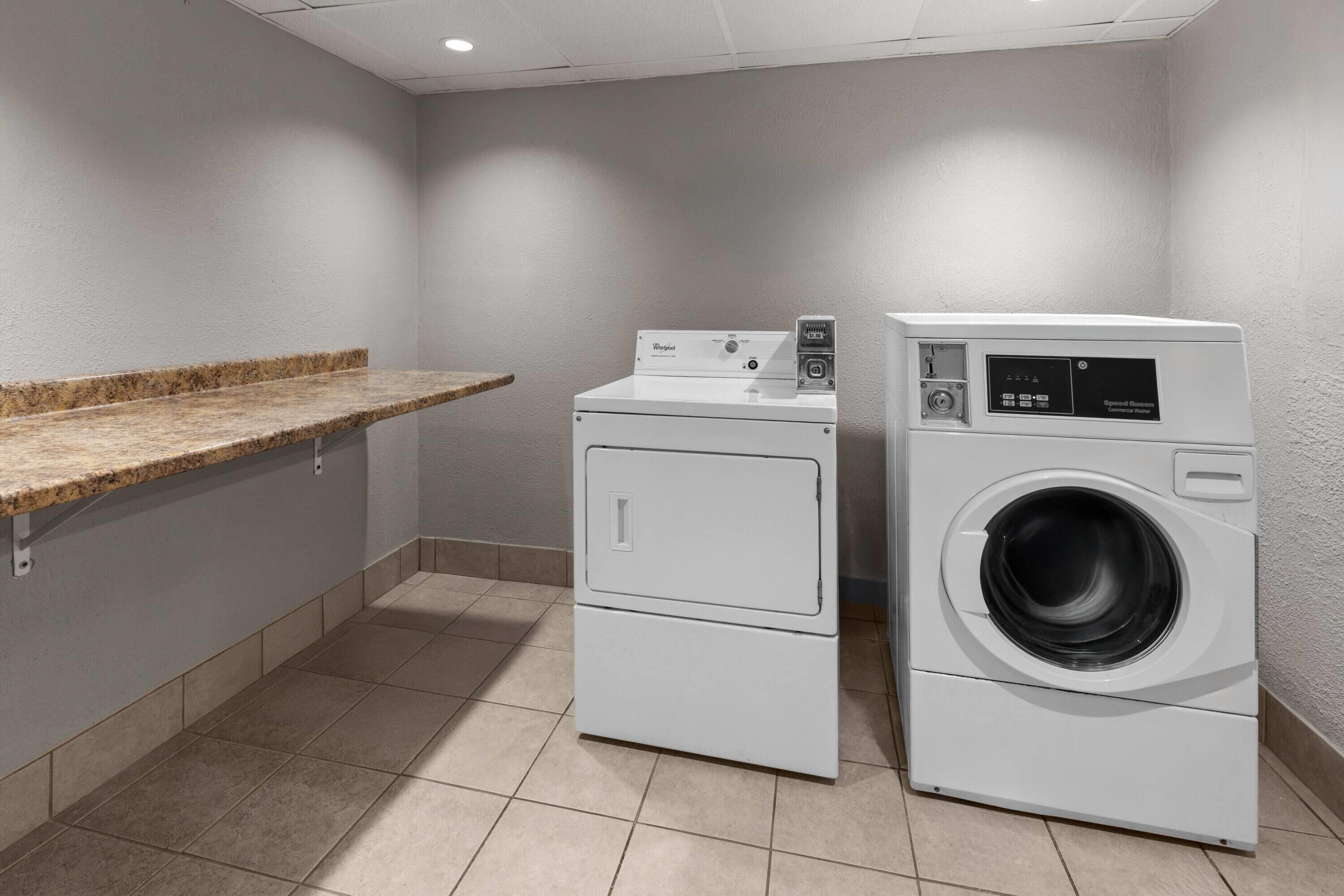A laundry room with a washing machine and dryer, a countertop, and tiled flooring.