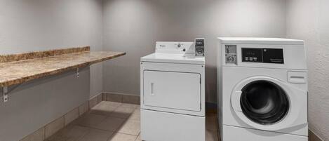 A laundry room with a washing machine and dryer, a countertop, and tiled flooring.