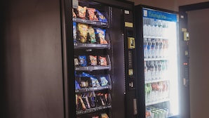 Dos máquinas expendedoras en un pasillo, una con aperitivos y la otra con bebidas.