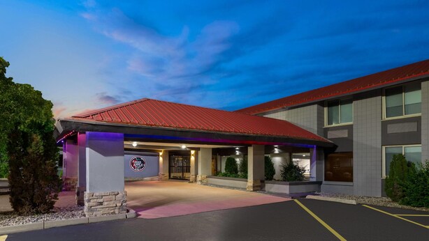 A hotel entrance with a red roof, a signboard, and a paved driveway.