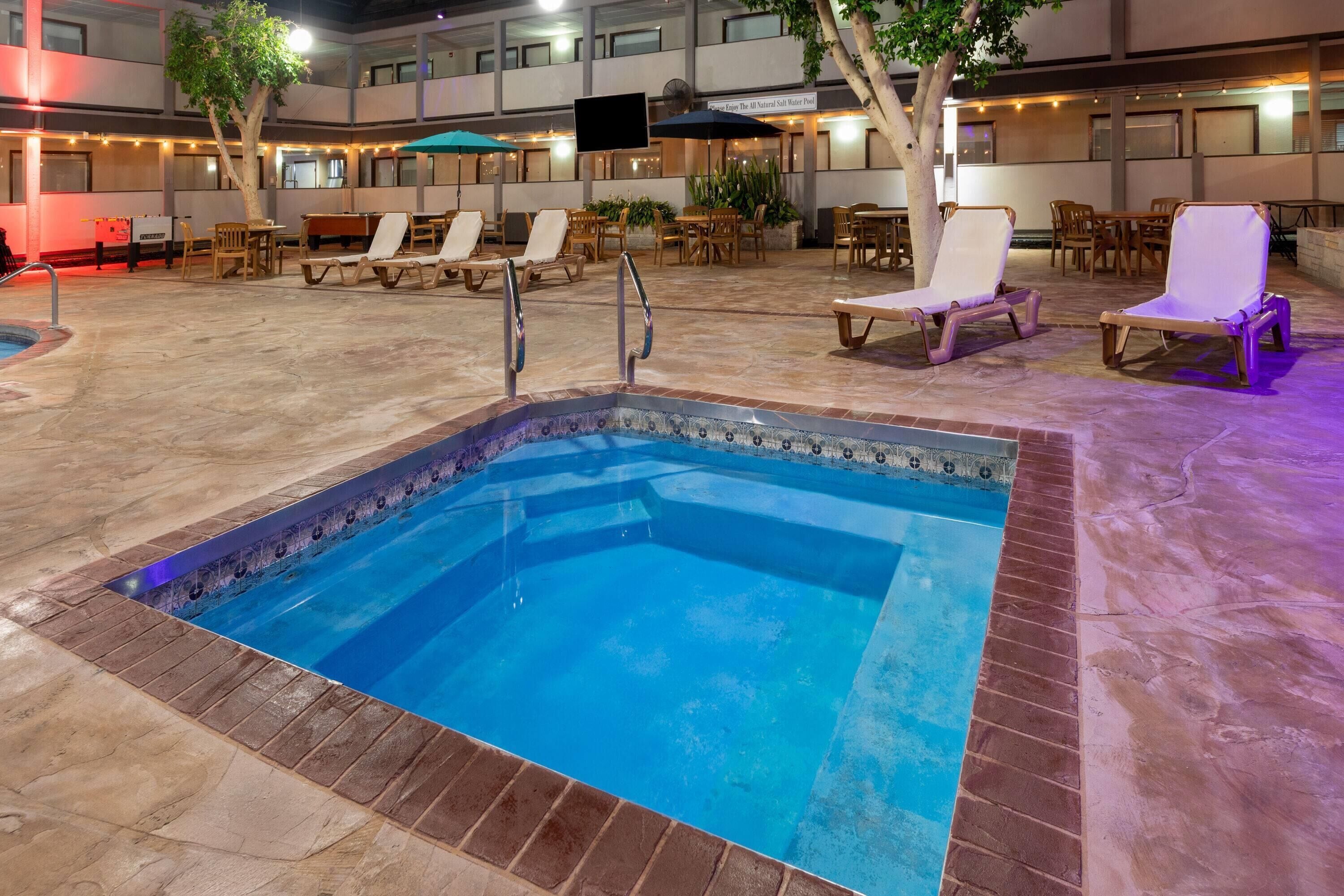 Una piscina con borde de azulejos y marco de ladrillo, rodeada de sillas de descanso y mesas.