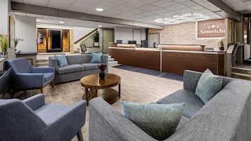 Un vestíbulo de hotel con mostrador de recepción, zona de estar y una escalera que conduce a un piso superior.