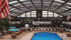 An indoor pool area with two pools, lounge chairs, and American flags.