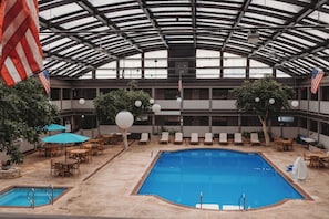 An indoor pool area with two pools, lounge chairs, and American flags.