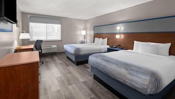 A hotel room with two beds, a desk, a chair, a lamp, and a window.
