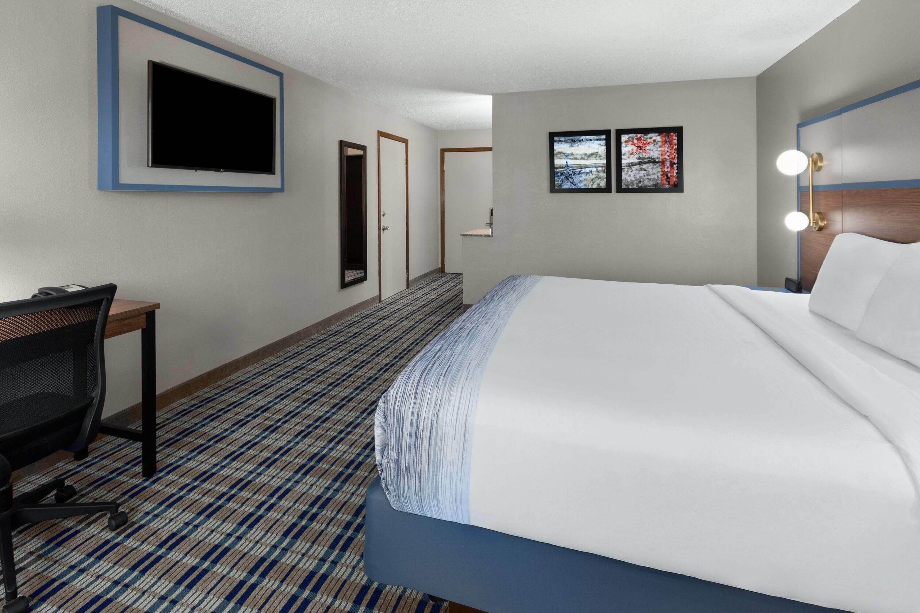 A hotel room with a bed, a desk, a chair, a television, and two framed pictures on the wall.