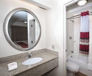 Een badkamer met een granieten blad, een ronde spiegel, een wit wastafelmeubel, een toilet en een douche met een gestreept gordijn.