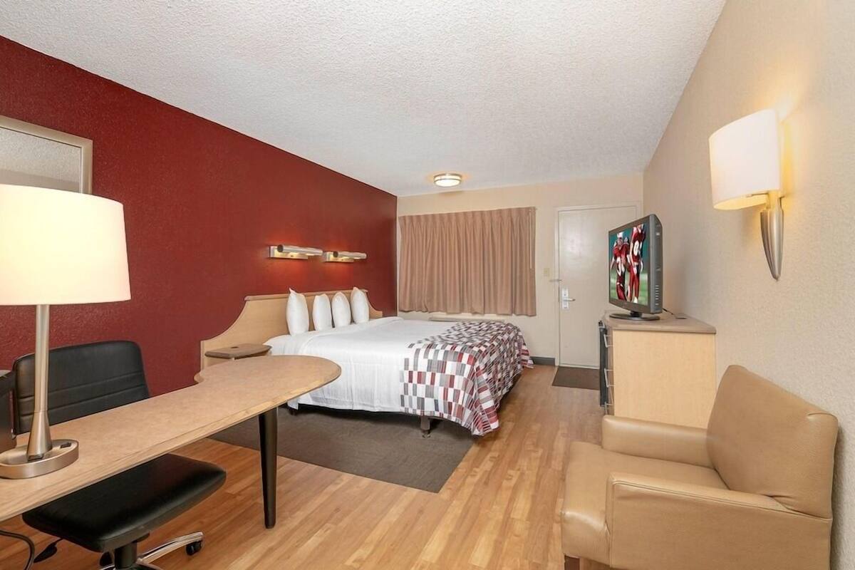 A hotel room with a bed, a desk with a lamp, a chair, a television, and a painting on the wall.