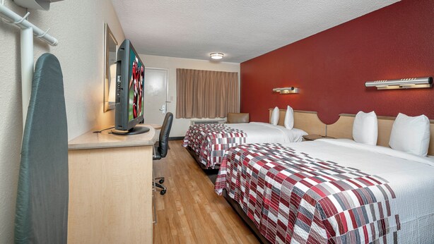 A hotel room with a desk, two beds, a chair, a TV, and a red accent wall. - Red Roof Inn Philadelphia - Oxford Valley (Langhorne)