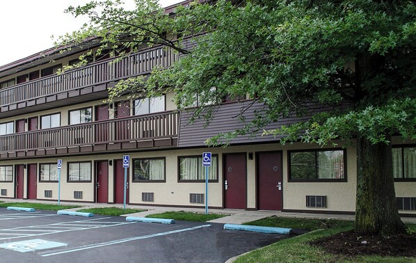 Un hôtel à plusieurs étages doté d’un parking, de panneaux indiquant les places réservées aux personnes handicapées et d’un arbre à l’avant.