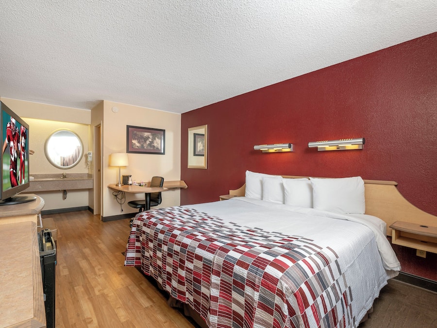 Quarto de hotel com cama, televisão, escrivaninha e espelho.