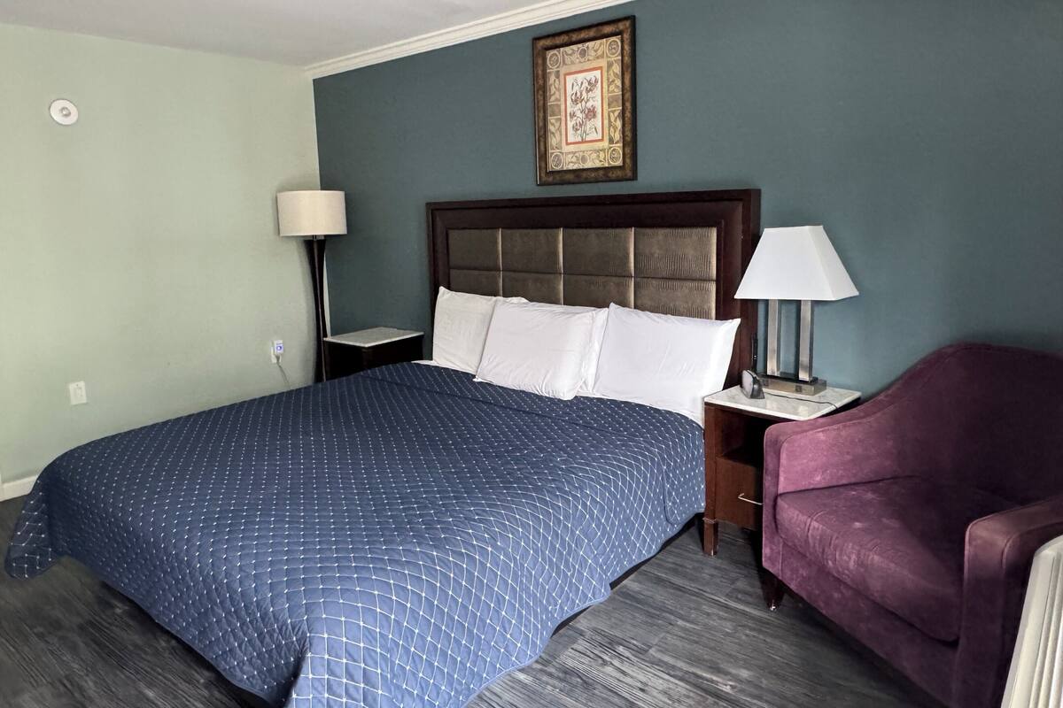 A hotel room with a large bed, two bedside tables, a chair, and a framed picture on the wall.