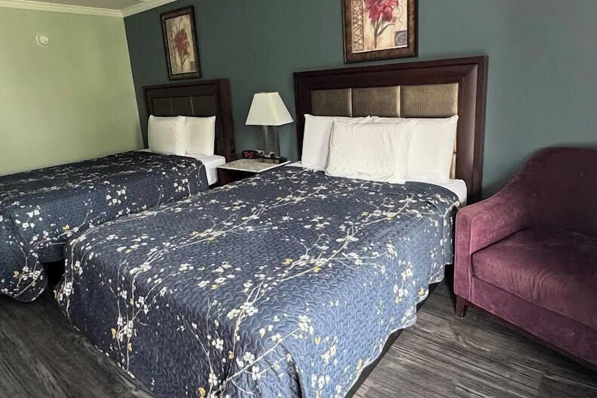 A hotel room with two beds, a nightstand, a lamp, a chair, and floral artwork on the walls.