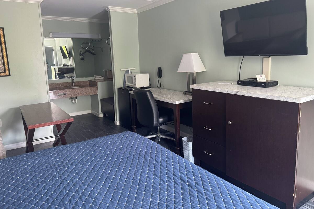 A hotel room with a bed, a desk, a chair, a television, and a microwave.