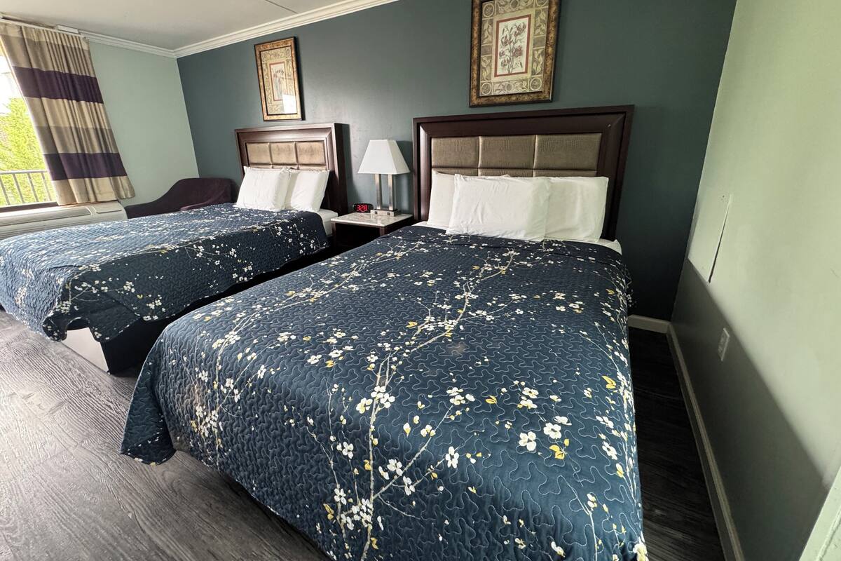 A hotel room with two beds, a nightstand, a lamp, and a framed picture on the wall.