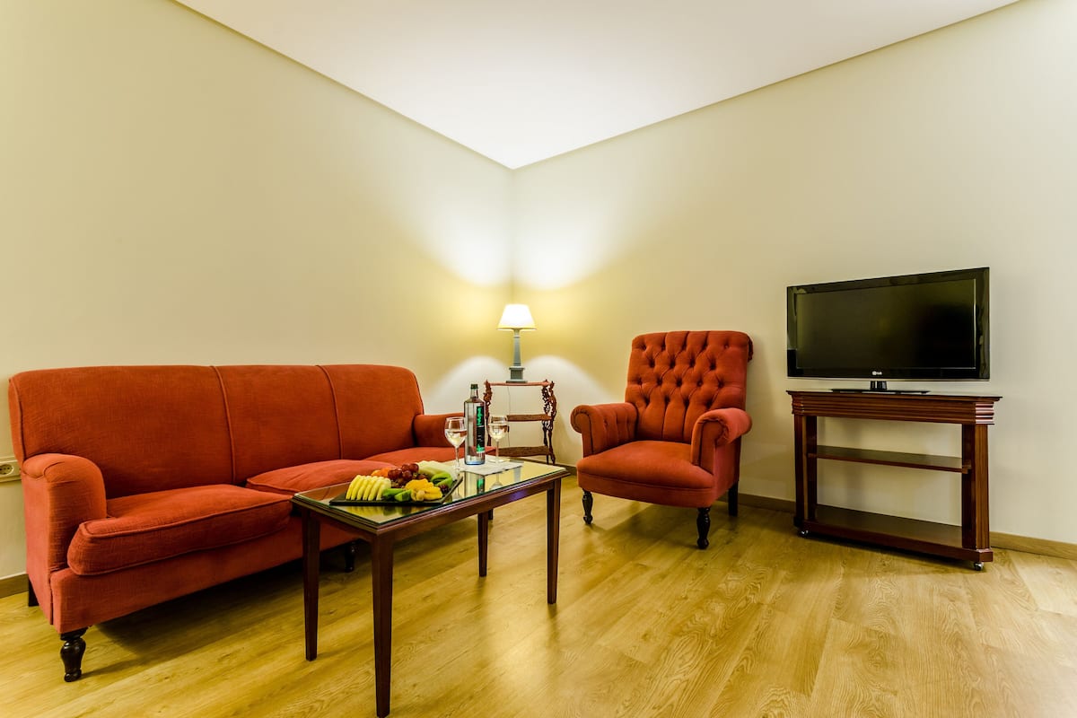 A living room with a red sofa, a wooden coffee table with fruits, a lamp, and a TV on a wooden stand.