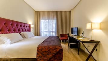 A hotel room with a large bed, a desk with a computer, a TV, and a lamp.