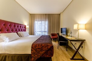 A hotel room with a large bed, a desk with a computer, a TV, and a lamp.
