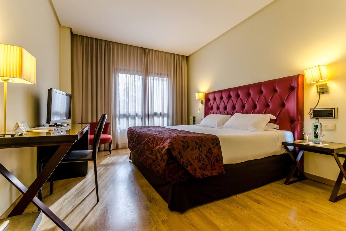 A hotel room with a large bed, a desk with a computer, a chair, and a television.