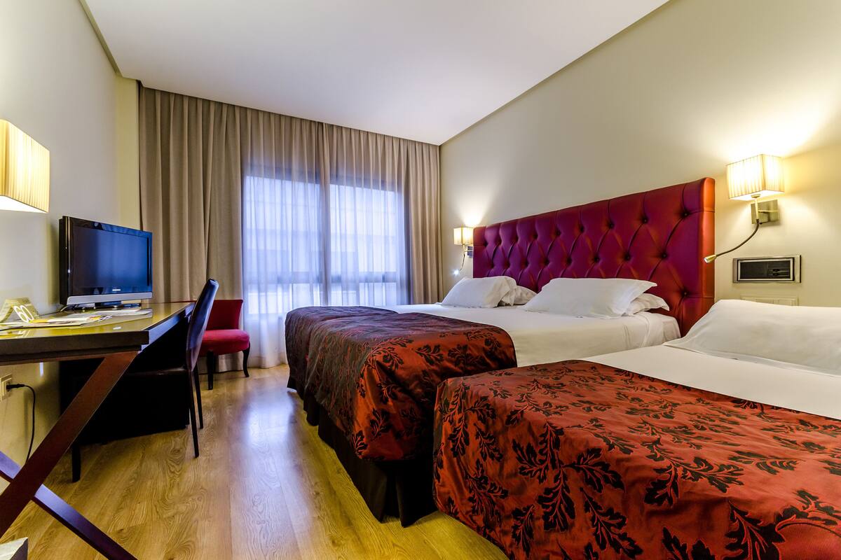 A hotel room with two beds, a desk with a computer, and a TV.