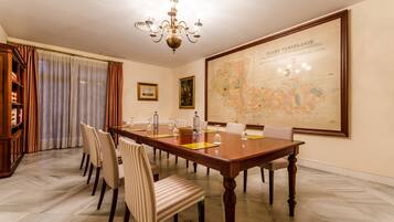 Una sala conferenze con un grande tavolo di legno, diverse sedie, un lampadario, una mappa appesa al muro e una libreria.