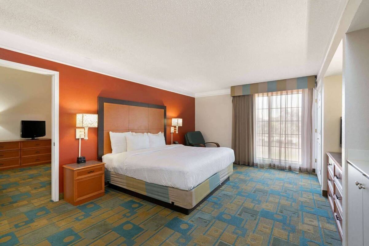 Een hotelkamer met een groot bed, bedlampen, een televisie op een dressoir en een raam met gordijnen.