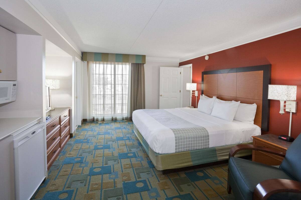 Een hotelkamer met een bed, een bureau, een stoel, een magnetron en een raam met gordijnen.