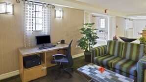 Et hotelværelse med skrivebord, computer, stol, sofa og en potteplante.
