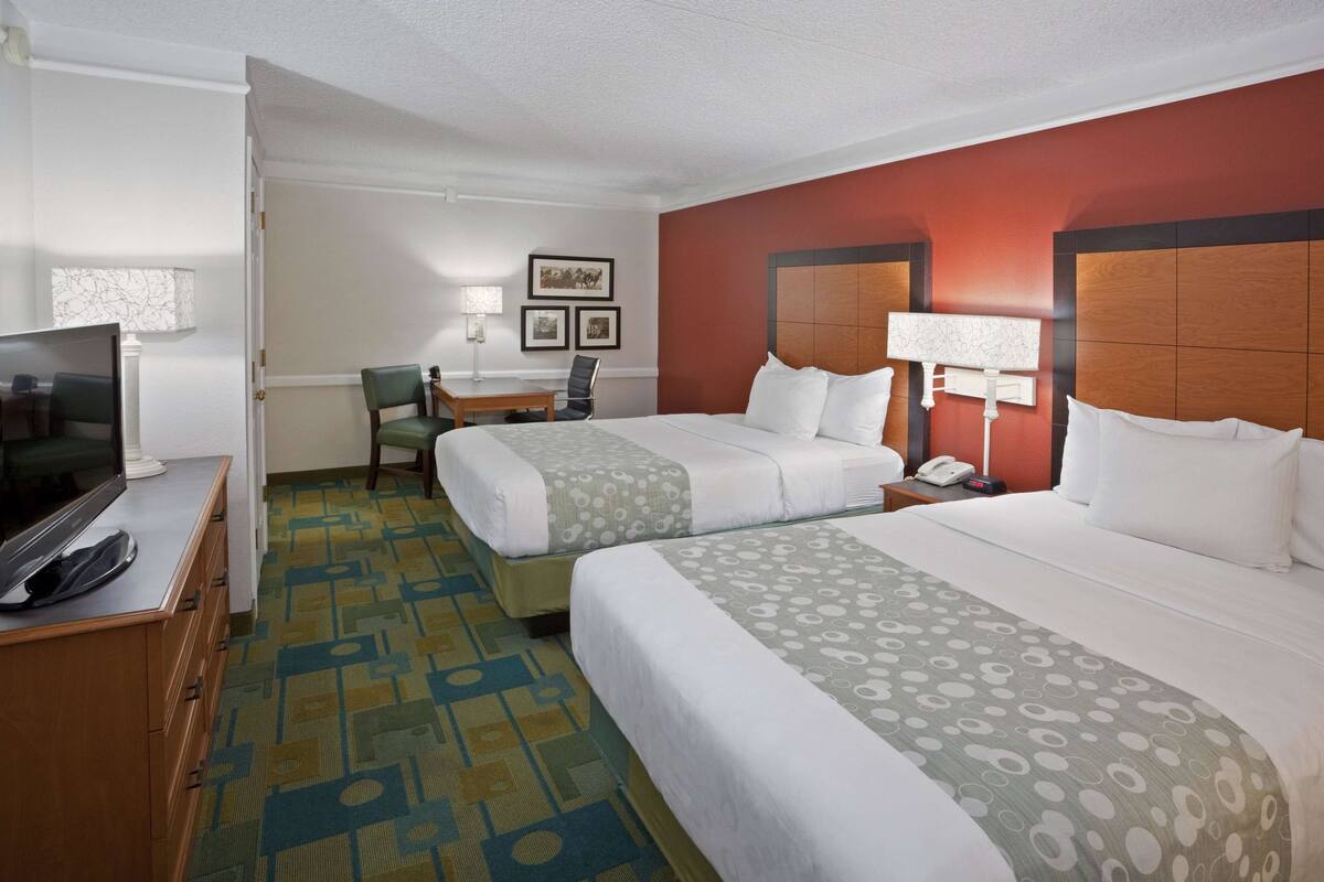 Een hotelkamer met twee bedden, een bureau, een stoel, een televisie en een kamerbreed tapijt met een patroon.