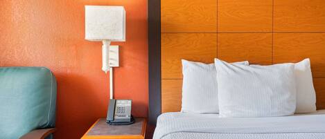 Habitación de hotel con cabecera de madera, mesita de noche con lámpara, teléfono y sillón verde.