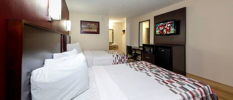 A hotel room with two beds, a desk, a television, and a mirror.