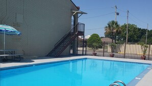 Una piscina rectangular con una escalera metálica en un lado, una mesa de picnic y un cartel que dice 'POOL RULES' en una pared de ladrillo.