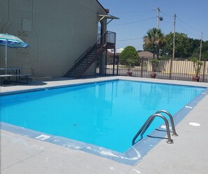 A rectangular swimming pool with a metal ladder on one side, a picnic table, and a 'POOL RULES' sign on a brick wall. - Red Roof Inn New Orleans - Westbank (Harvey)