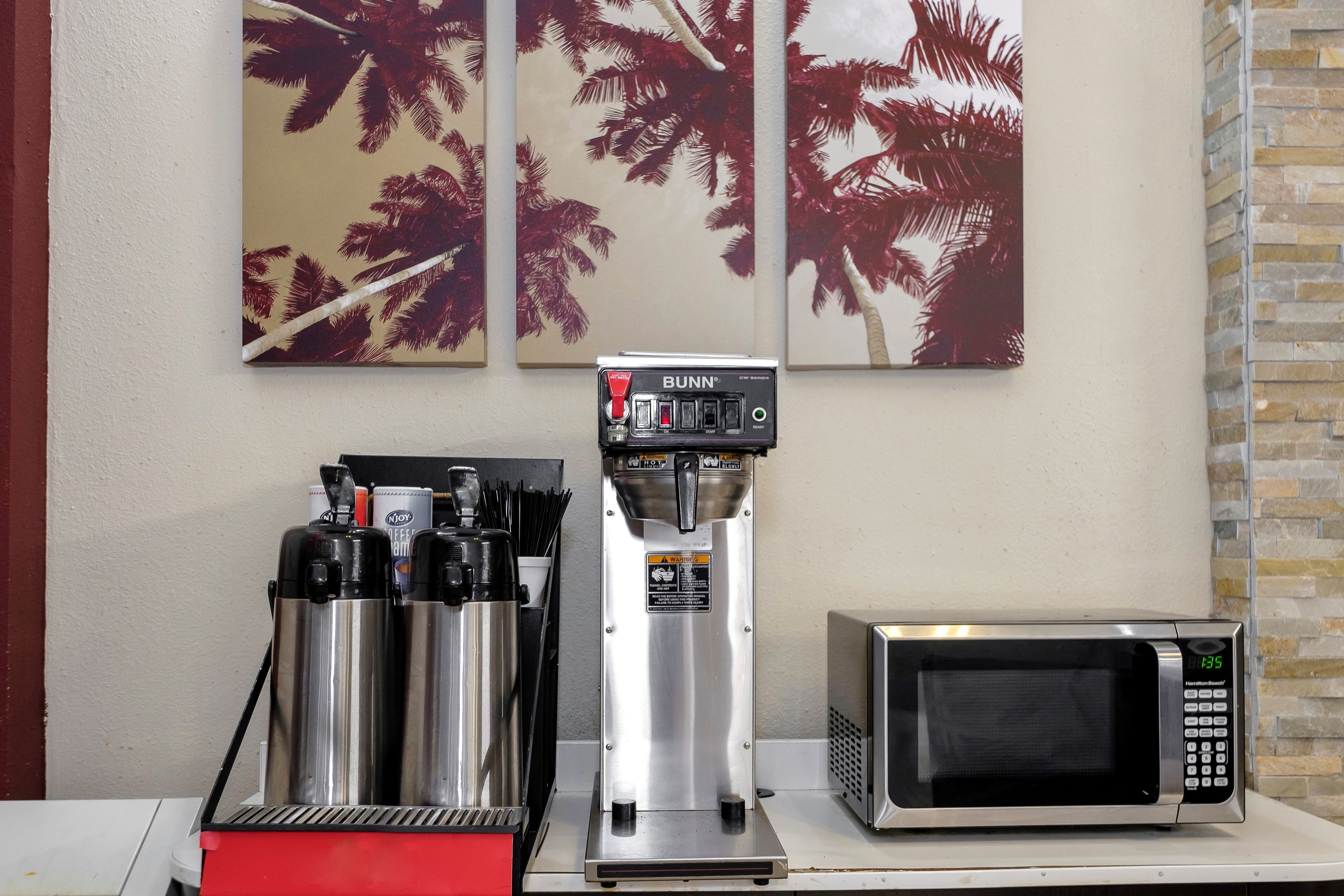 A coffee machine, a microwave, and two thermos flasks on a counter with palm tree artwork on the wall.