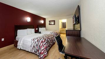 Quarto de hotel com uma cama grande, uma escrivaninha, uma cadeira, uma televisão e um banheiro visível por uma porta aberta.