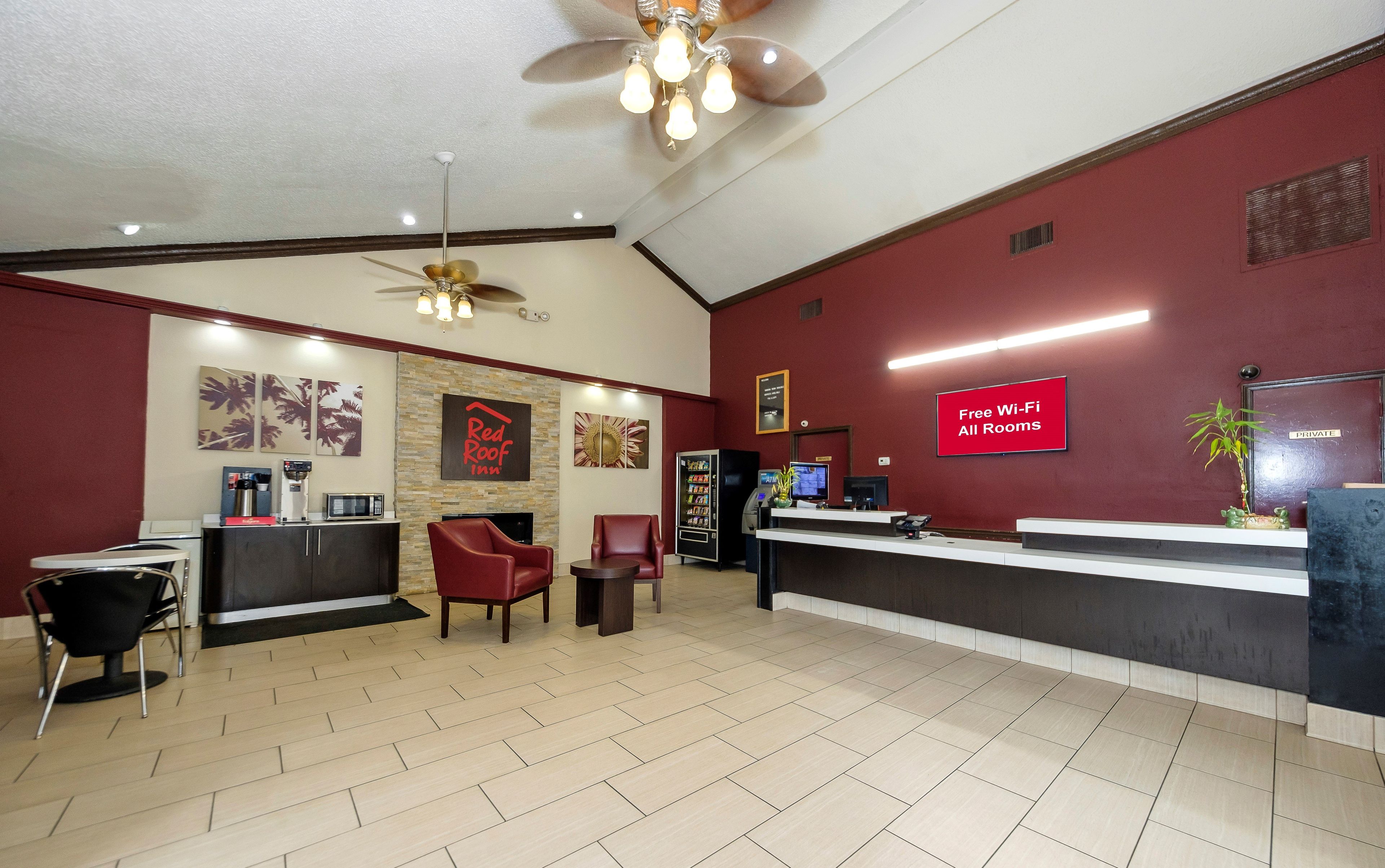A hotel reception area with a reception desk, seating, a vending machine, and a ceiling fan.